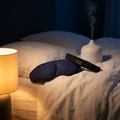 Masque chauffant, bandeau audio et diffuseur posés sur un lit en lin, lumière basse du soir
